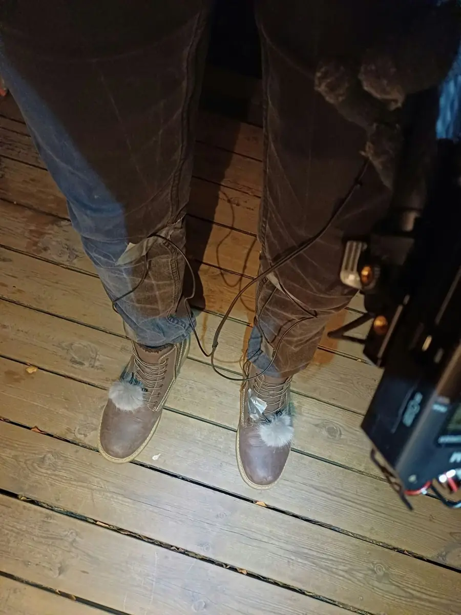 Boots with small microphones taped to the laces on a wooden deck