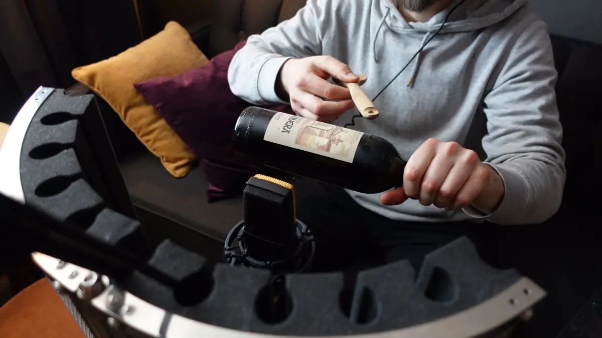 Tapping a wine bottle with a wooden spoon in front of a studio microphone