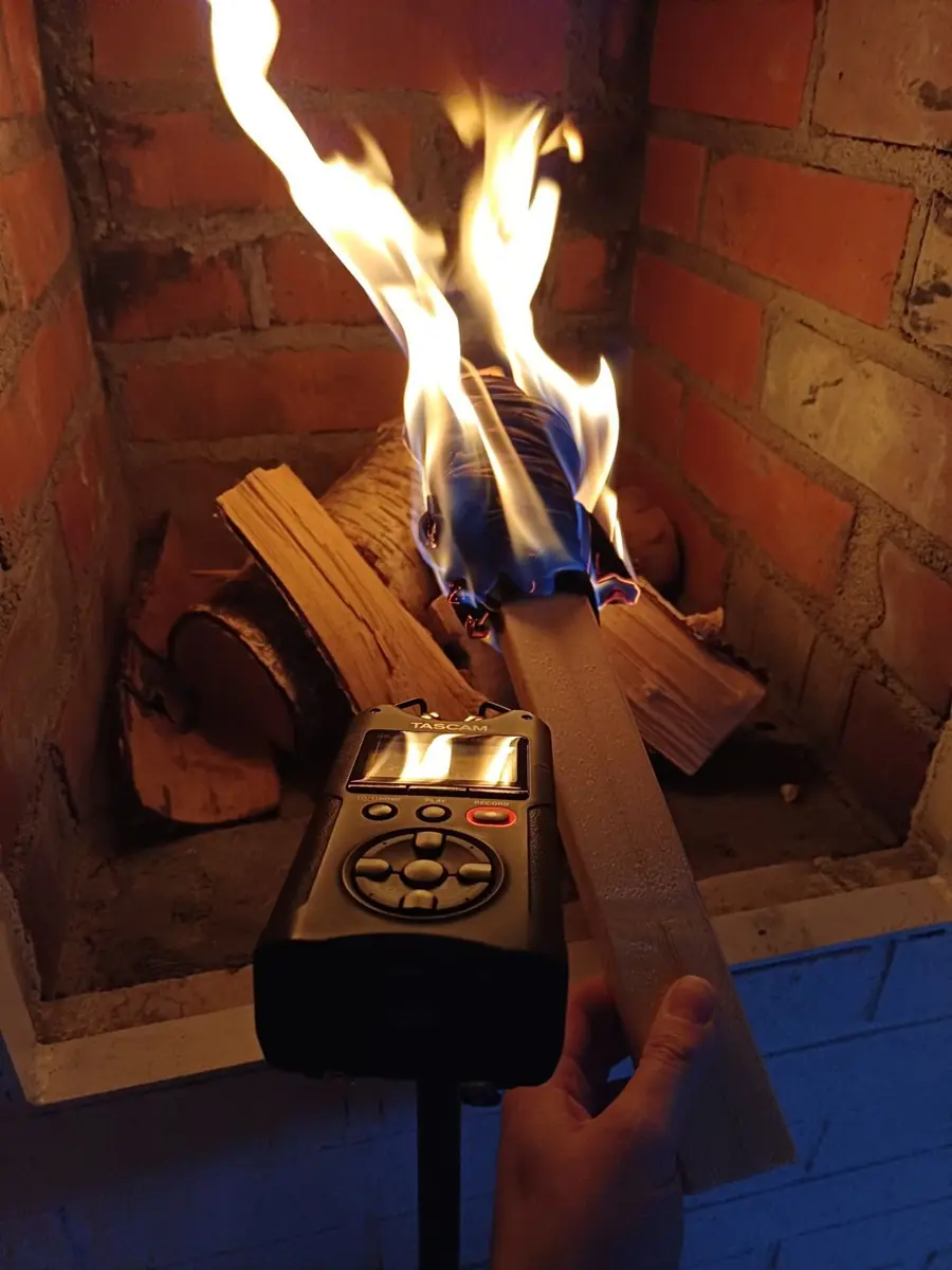 A handheld recorder held up to a burning torch in a brick fireplace